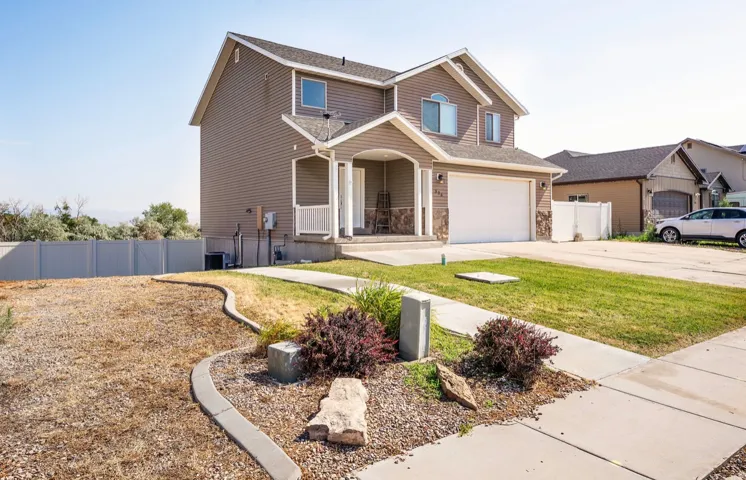 Two-story residence featuring a covered front porch with white railings, a two-car garage, and stone accent siding