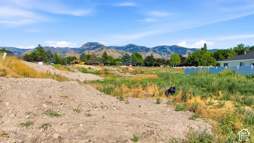 Expansive open lot with distant mountain scenery, bordered by natural vegetation and an adjacent white fence