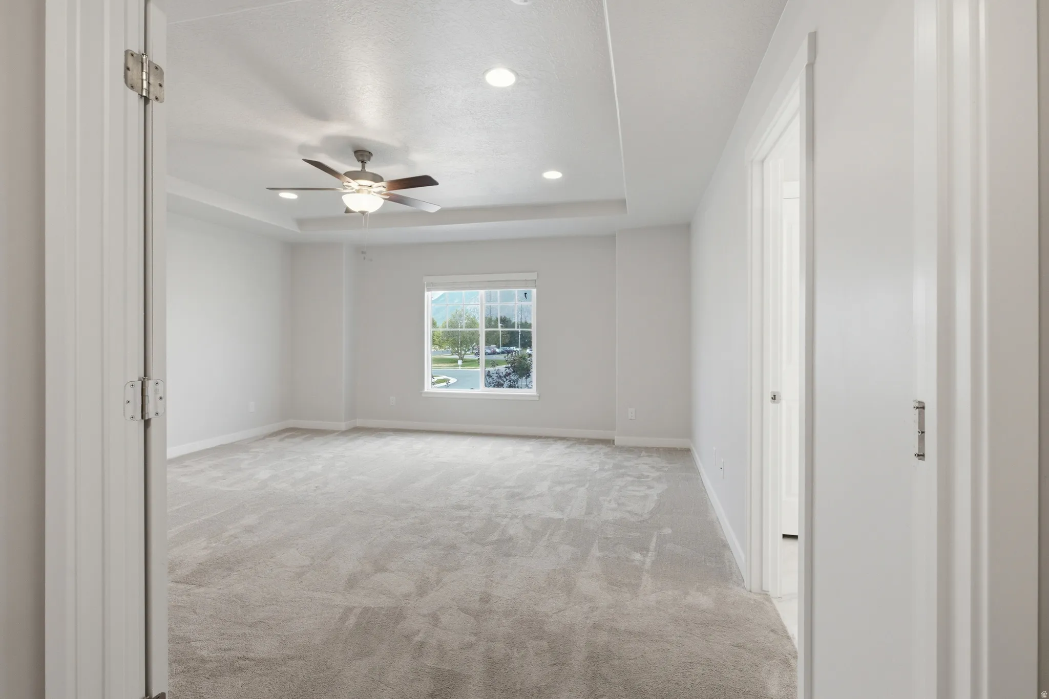 Spacious room featuring tray ceiling with recessed lighting, ceiling fan, and carpet flooring