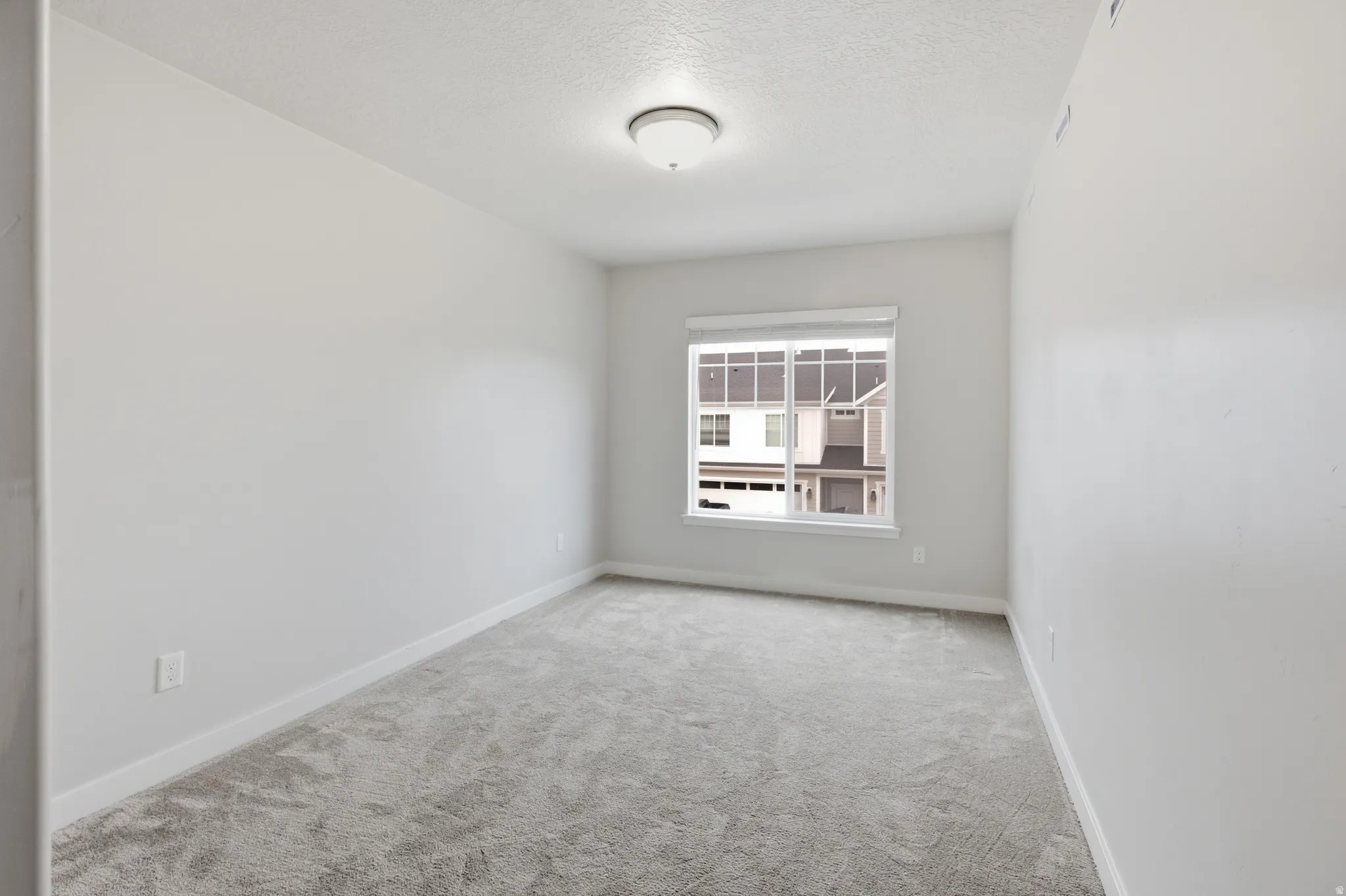 Carpeted room featuring a single window with a white frame, overhead flush mount lighting, and neutral wall tones