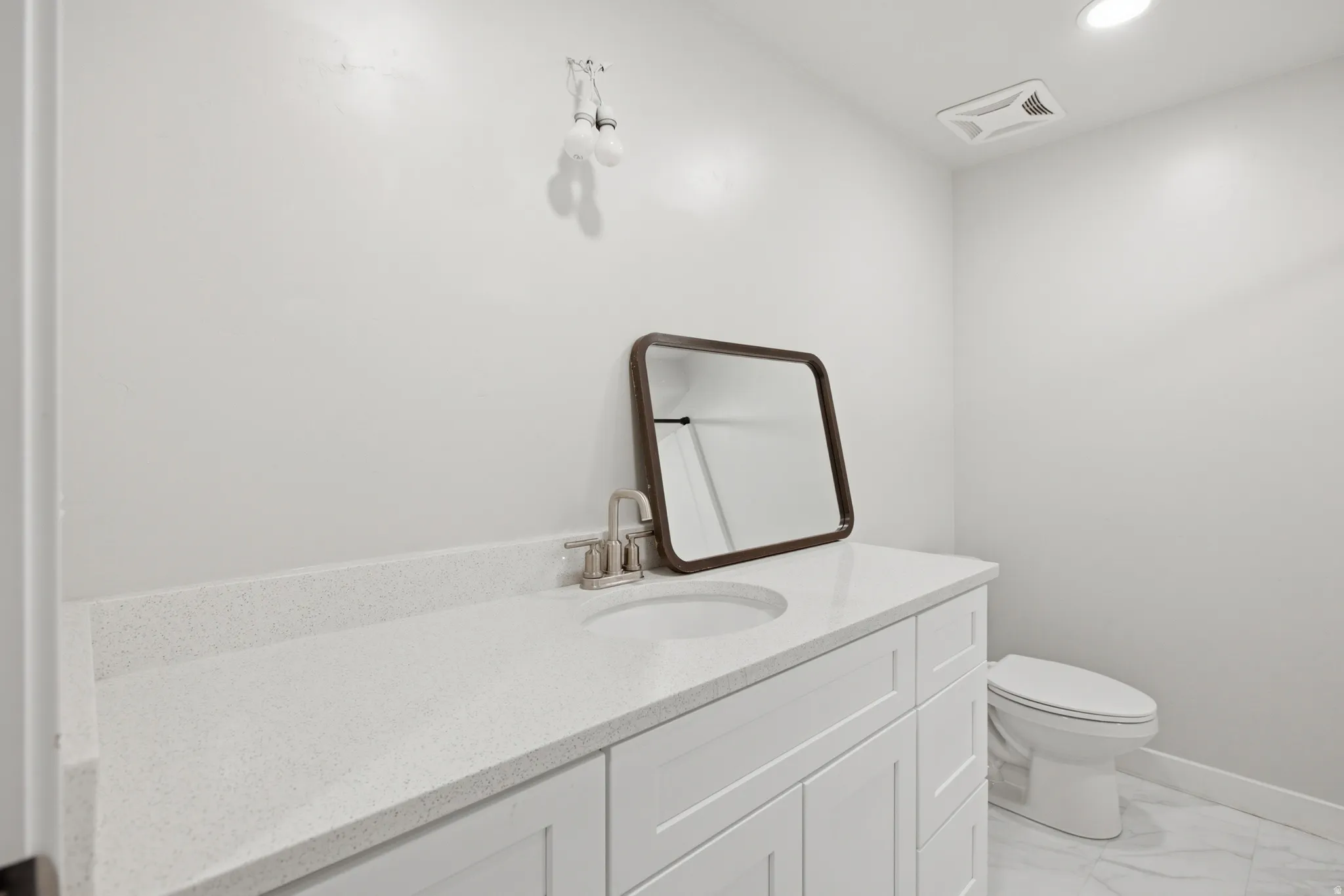 White vanity with a light speckled countertop, undermount sink, and brushed nickel faucet