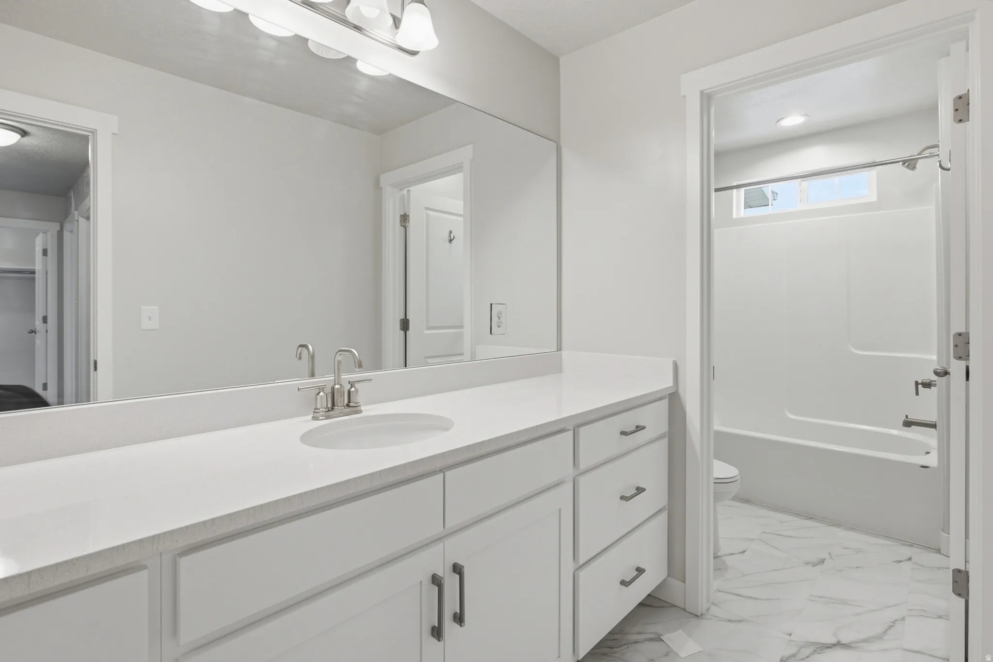 Bathroom vanity featuring a single undermount sink with brushed nickel faucet, light-toned countertop, and white cabinetry with dark pulls