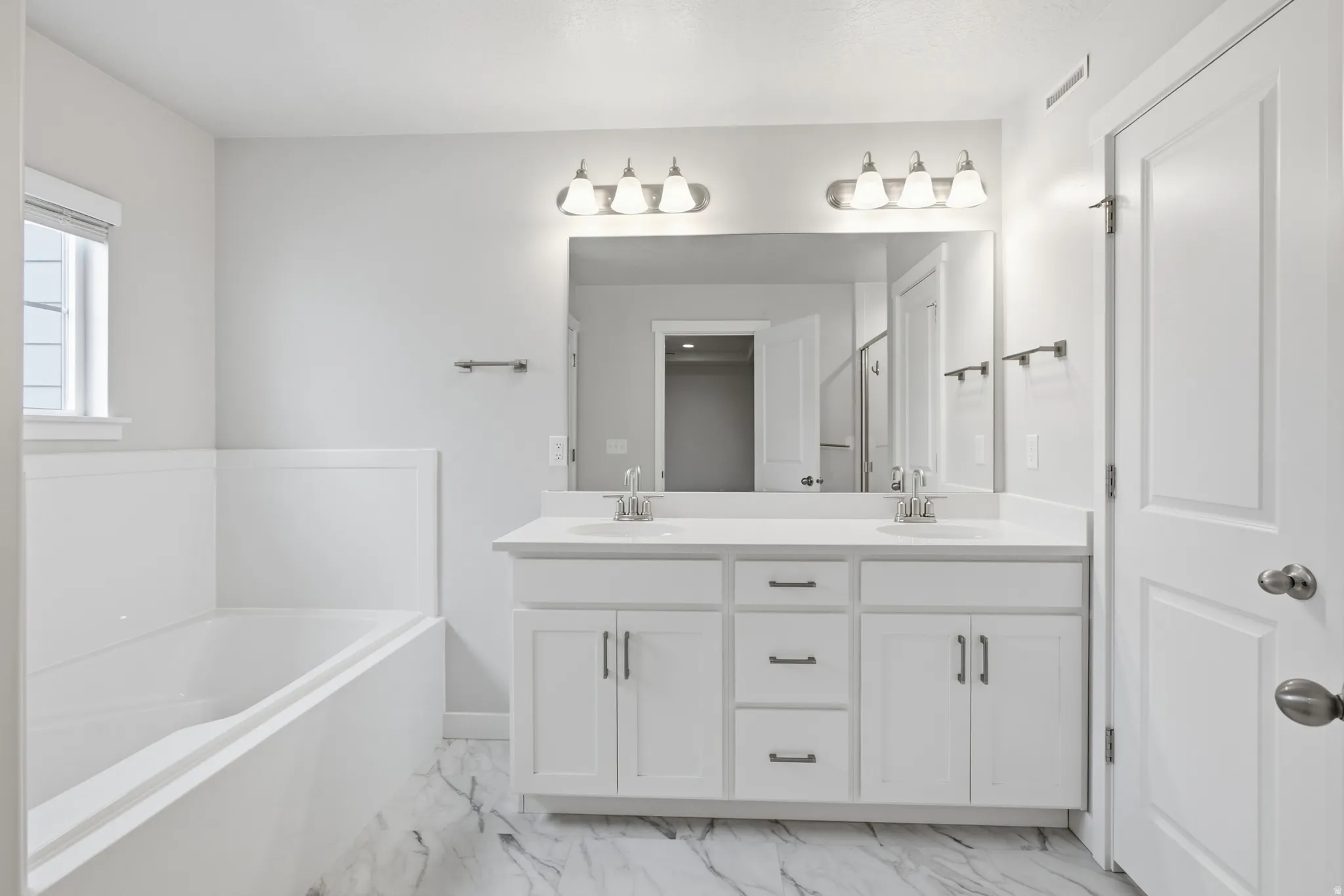 Double vanity with white cabinetry and integrated sinks, complemented by a large mirror and overhead light fixtures