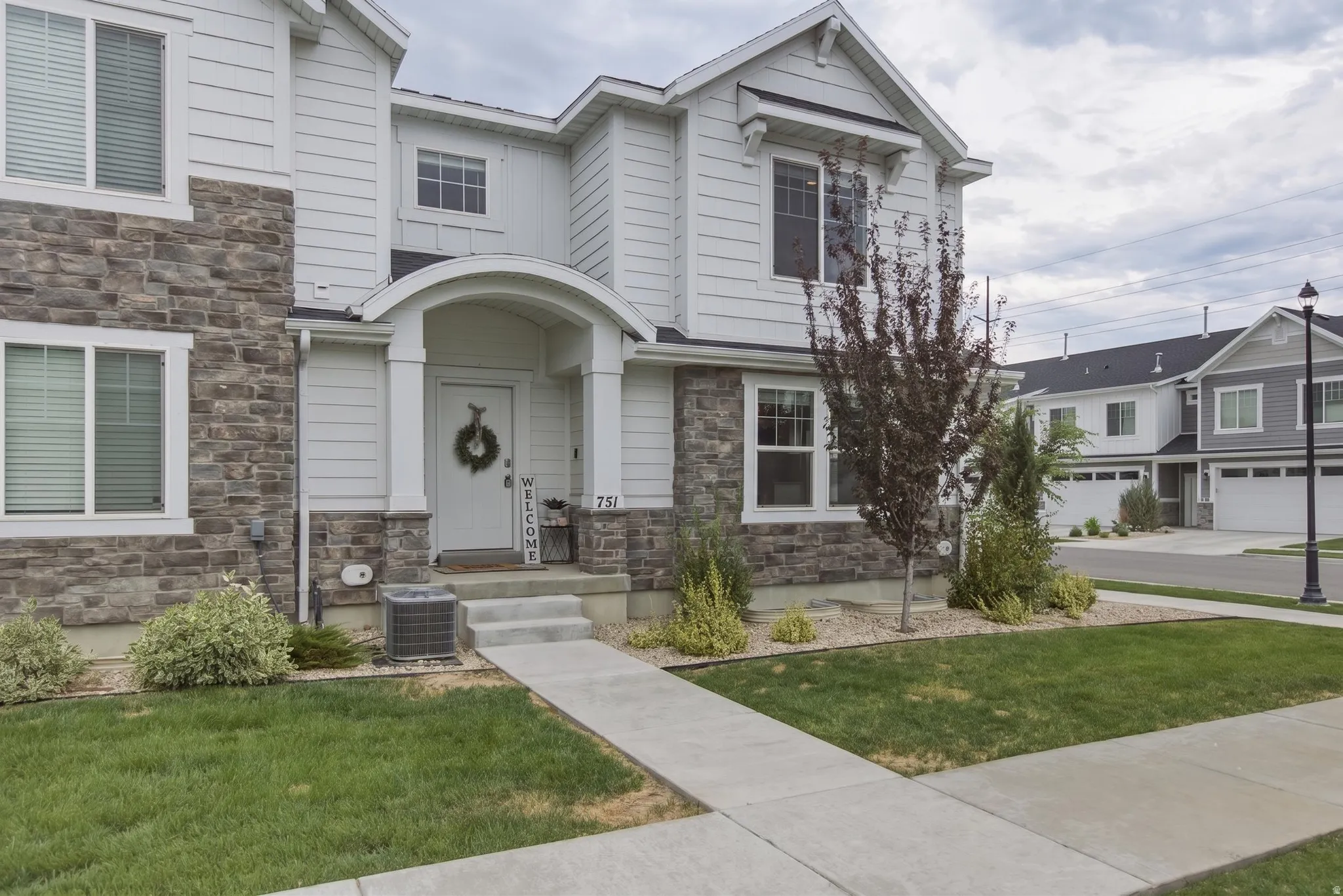 Two-story residence featuring a stone and horizontal siding exterior, an arched entry, and a concrete walkway