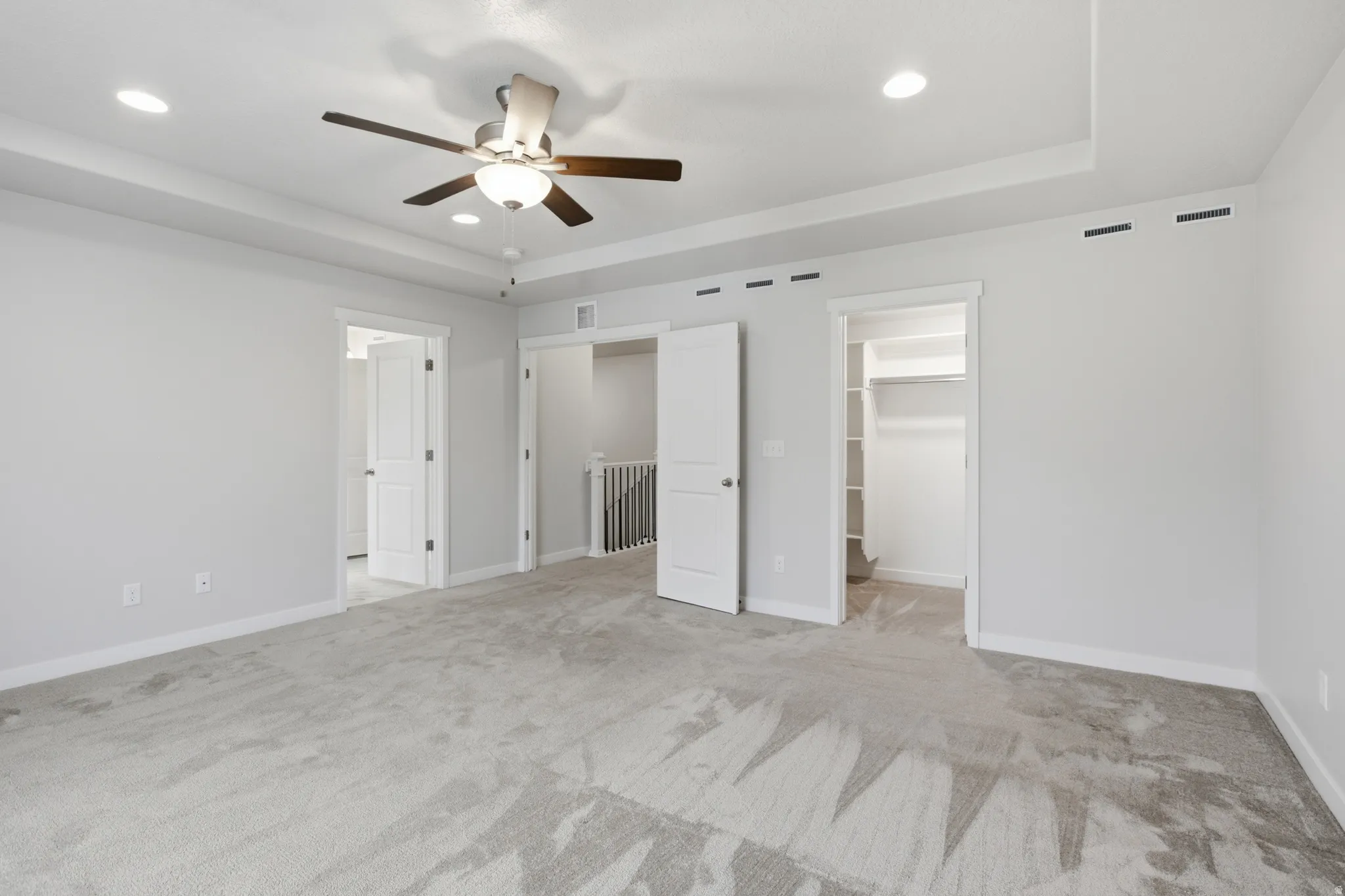Spacious room featuring tray ceilings with recessed lighting, a ceiling fan, and light gray carpeting