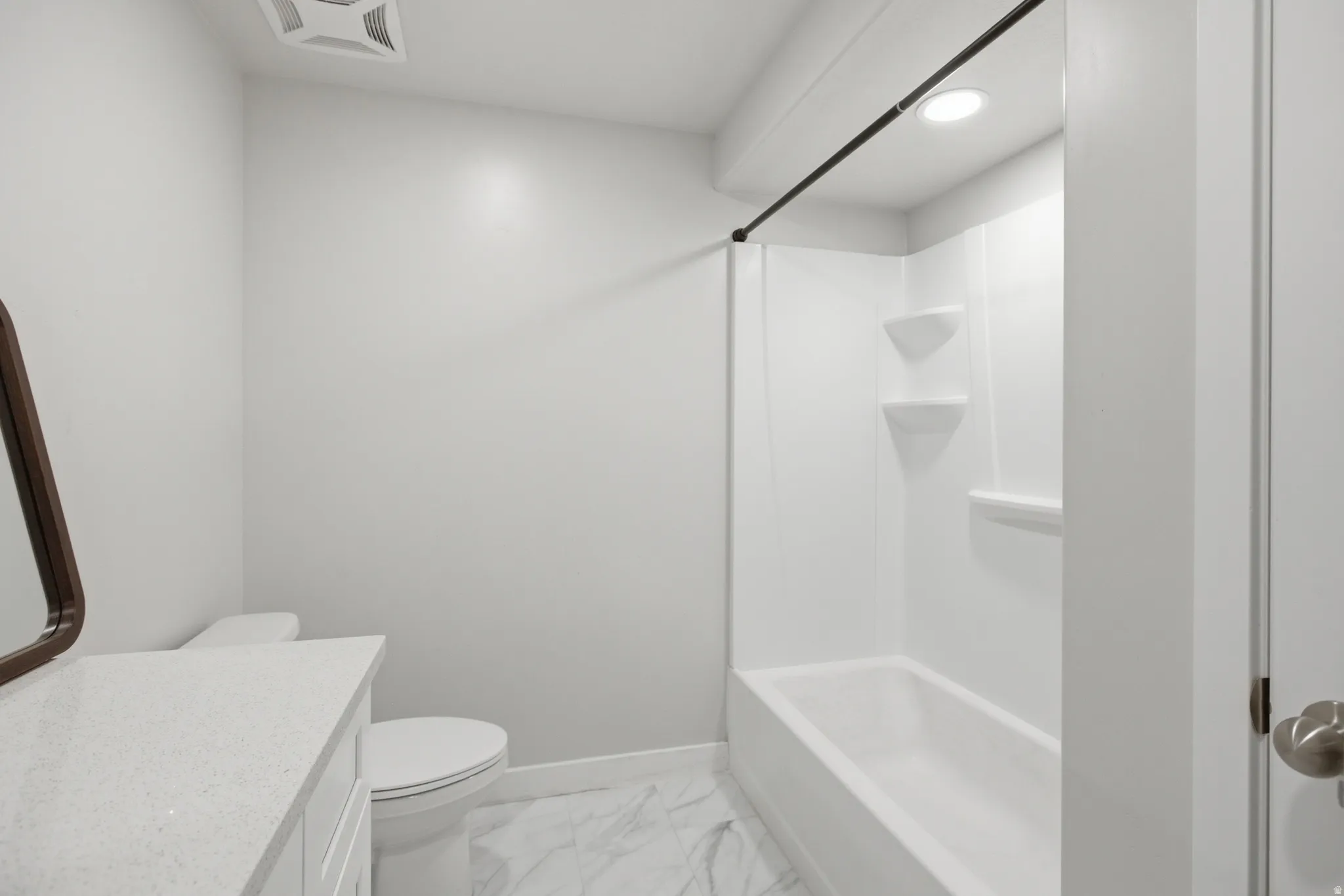 Bathroom featuring a white vanity with a light-toned countertop, a white toilet, and a white tub/shower combination with built-in shelving