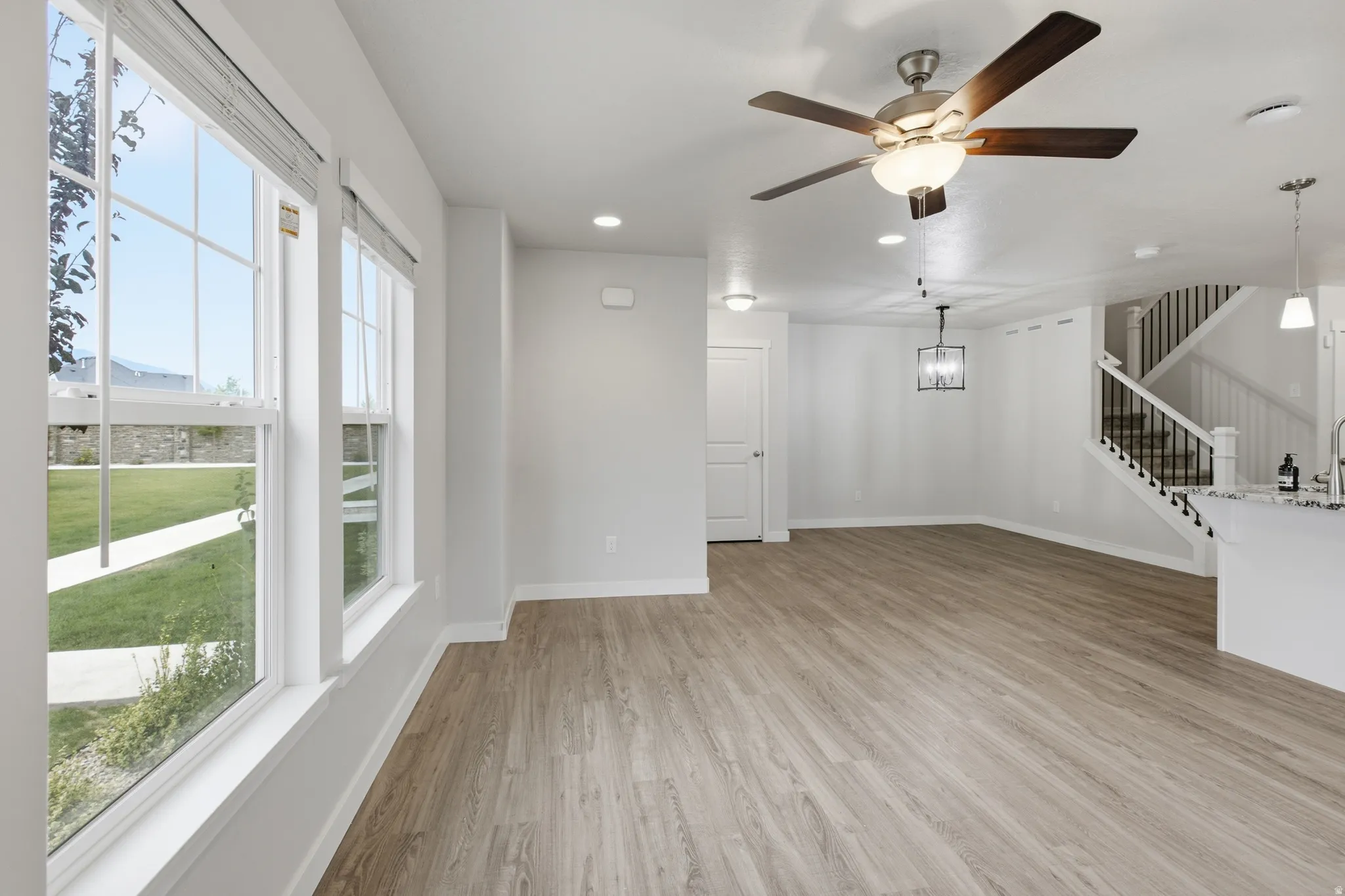 Open-concept living area featuring wood-finish flooring, a contemporary ceiling fan, and a built-in staircase with dark iron balusters