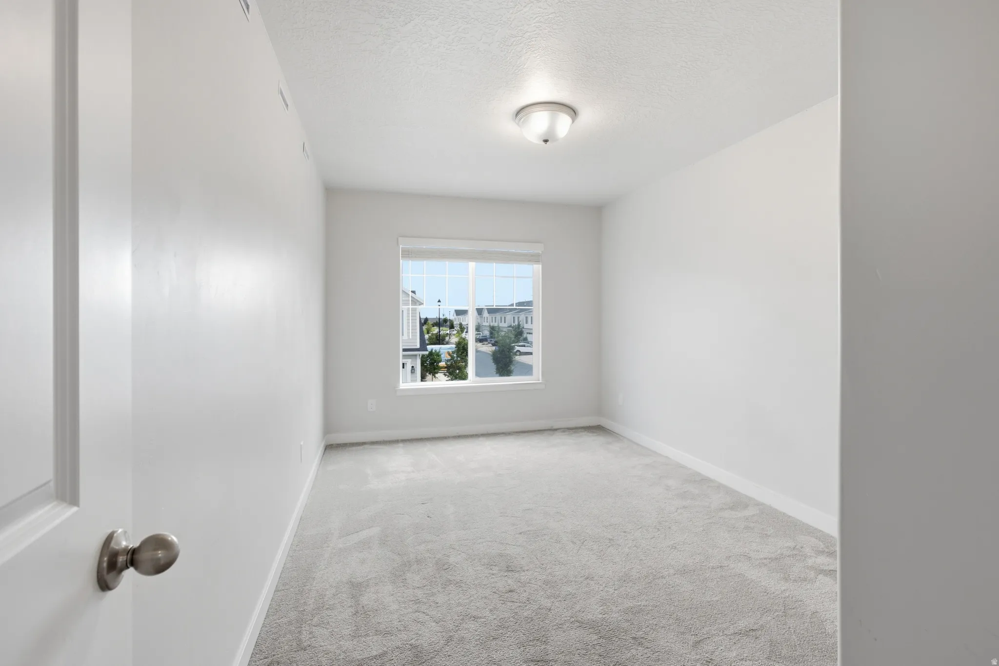 Light-filled room featuring neutral wall tones and a window overlooking the surrounding neighborhood