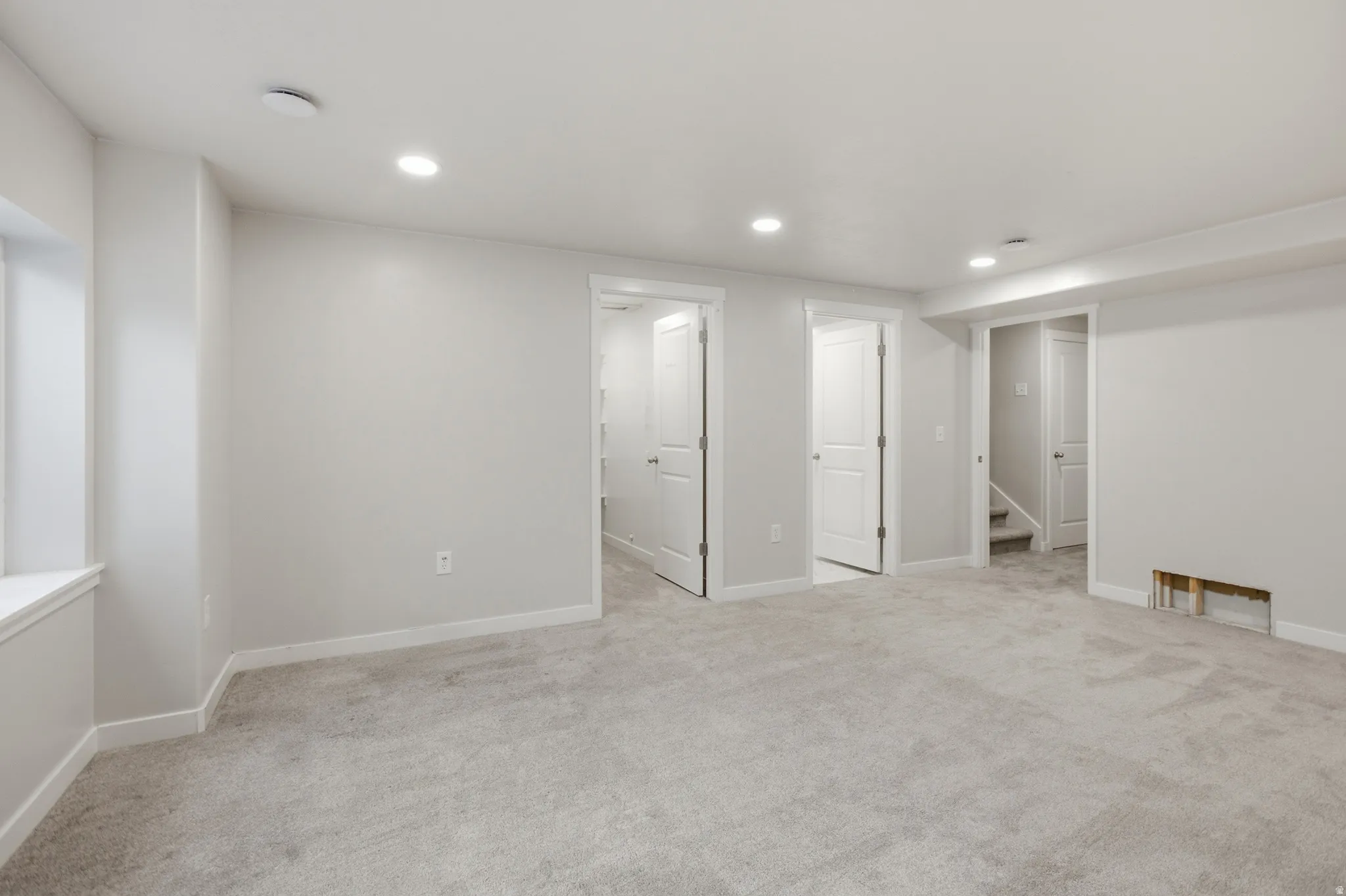 Spacious room featuring light gray carpeting, recessed lighting, white trim, and multiple white interior doors