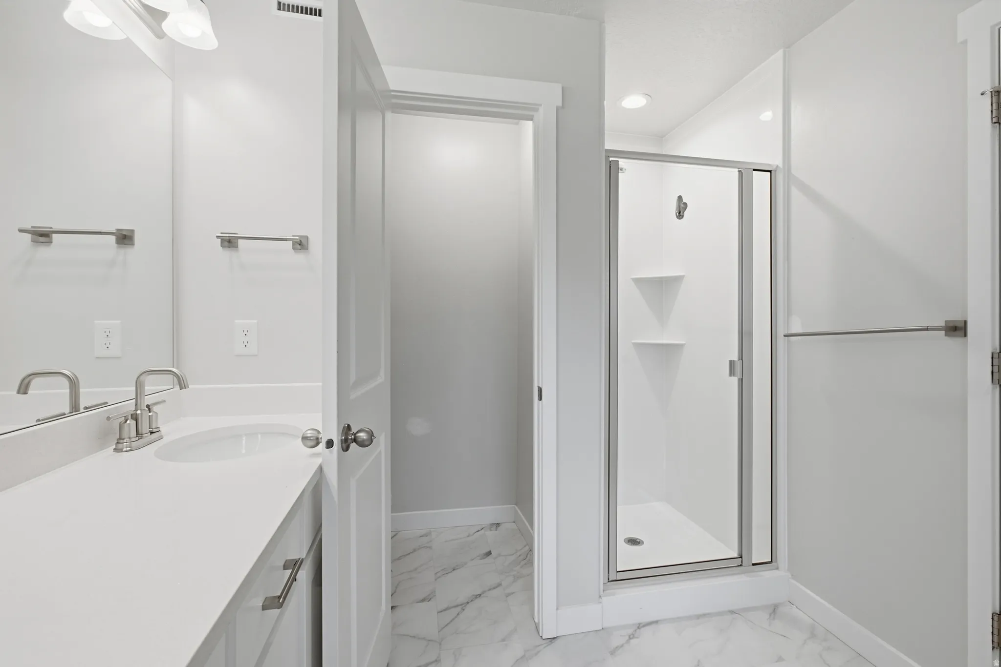 Bathroom featuring a single vanity with a white countertop and undermount sink, brushed nickel faucet, and frameless mirror
