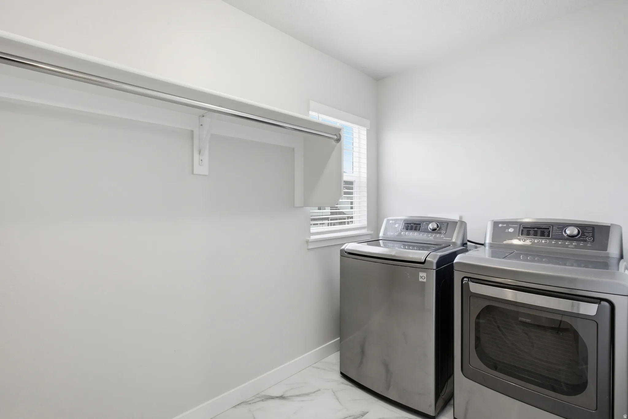Laundry area featuring white walls, marble-patterned flooring, a window with blinds, and an integrated hanging rod with shelving