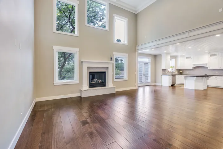 High ceilings and wood-finish flooring define this open concept living area, featuring a white mantle fireplace with a stone surround