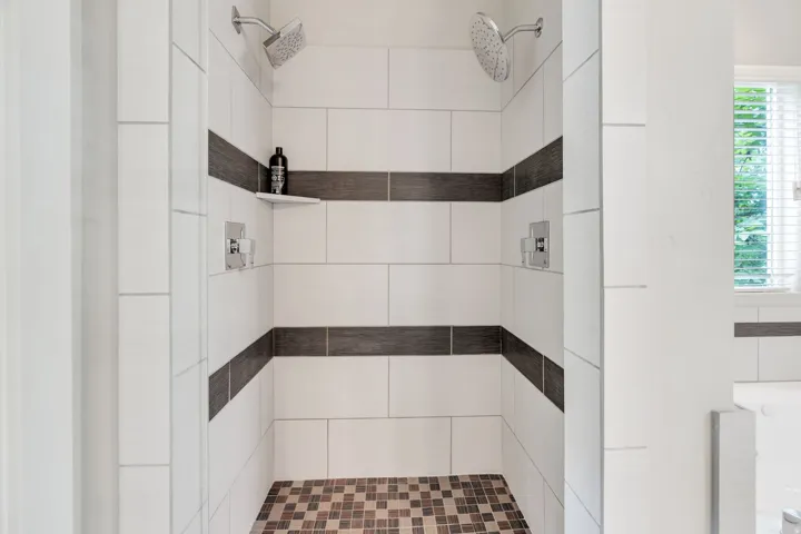 Walk-in shower with dual shower heads, white subway tile walls, and two horizontal accent bands of dark tile
