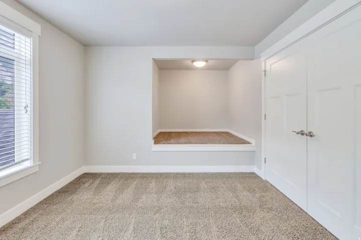 Built-in carpeted nook with overhead lighting, neutral carpet flooring, and a window featuring blinds