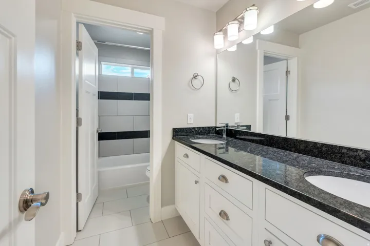 Dual vanity with a dark granite countertop, undermount sinks, and white shaker-style cabinetry