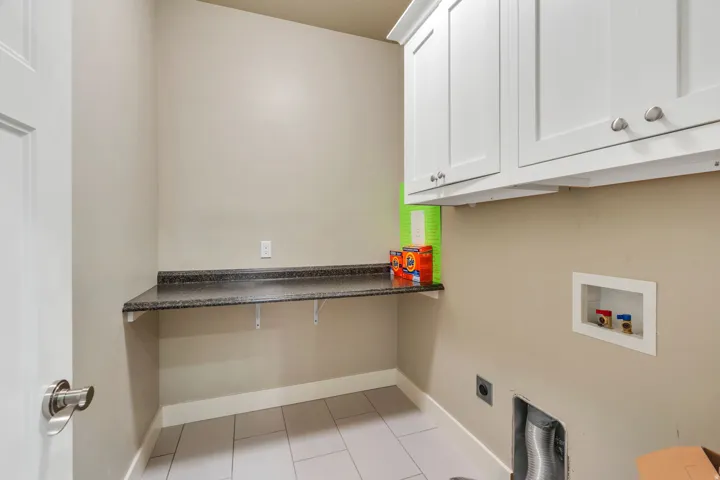 Dedicated utility room featuring light-toned walls, white shaker-style cabinetry, and a dark speckled countertop