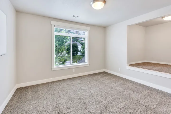 Spacious room featuring neutral carpeting, a large window with blinds, and a recessed platform area with additional lighting