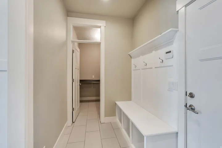 Entryway featuring built-in white bench seating with integrated storage, coat hooks, and durable tile flooring