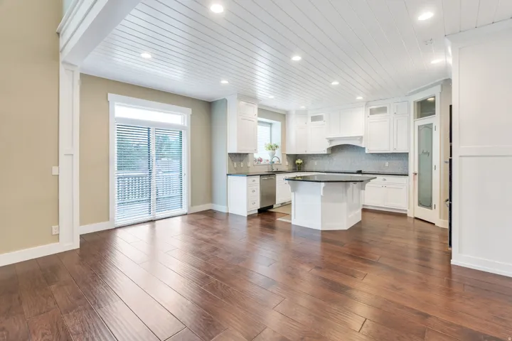Open-concept kitchen and living area featuring wood-finish flooring, white cabinetry, a kitchen island with a dark countertop, and a white plank ceiling with recessed lighting