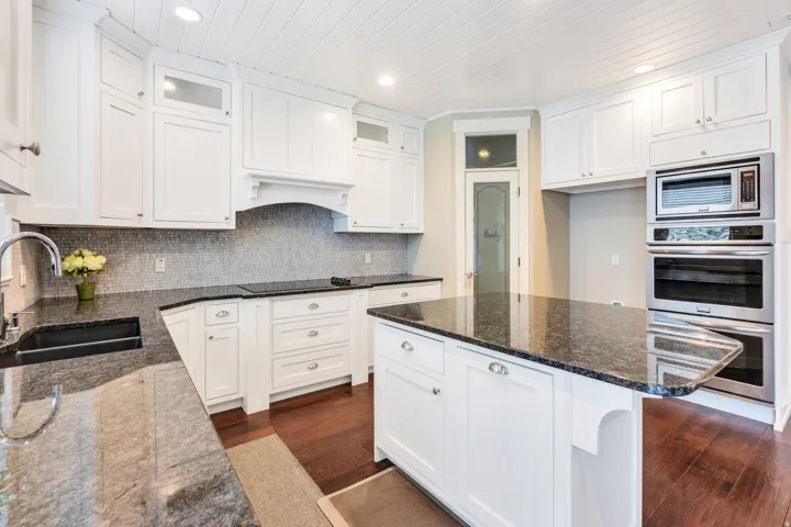 Kitchen featuring white cabinetry, dark granite countertops, stainless steel appliances, wood-finish flooring, and a tiled backsplash