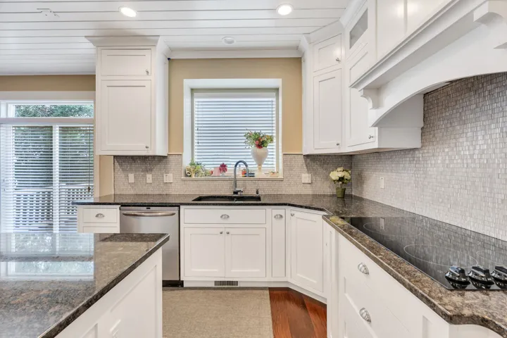 Kitchen featuring white shaker cabinetry, dark granite countertops, stainless steel dishwasher, and a mosaic tile backsplash