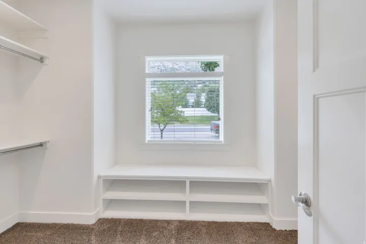 Walk-in closet featuring built-in shelving, hanging rods, and a window with blinds