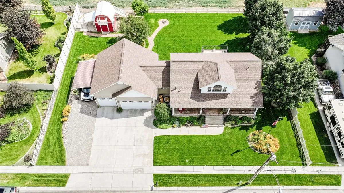 Expansive property featuring a meticulously manicured lawn, an attached two-car garage, covered front porch, and a gravel side parking area with an attached carport