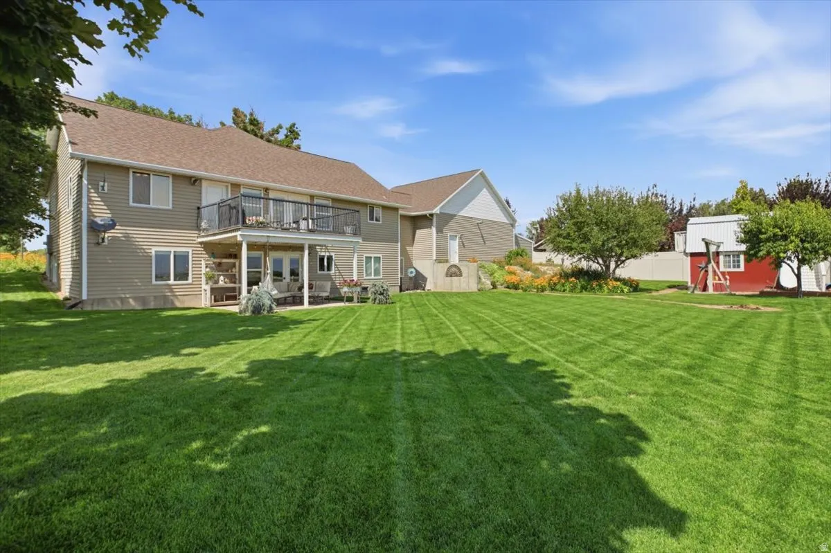 Expansive green lawn with a two-story beige siding residence featuring a second-story balcony and a covered patio below