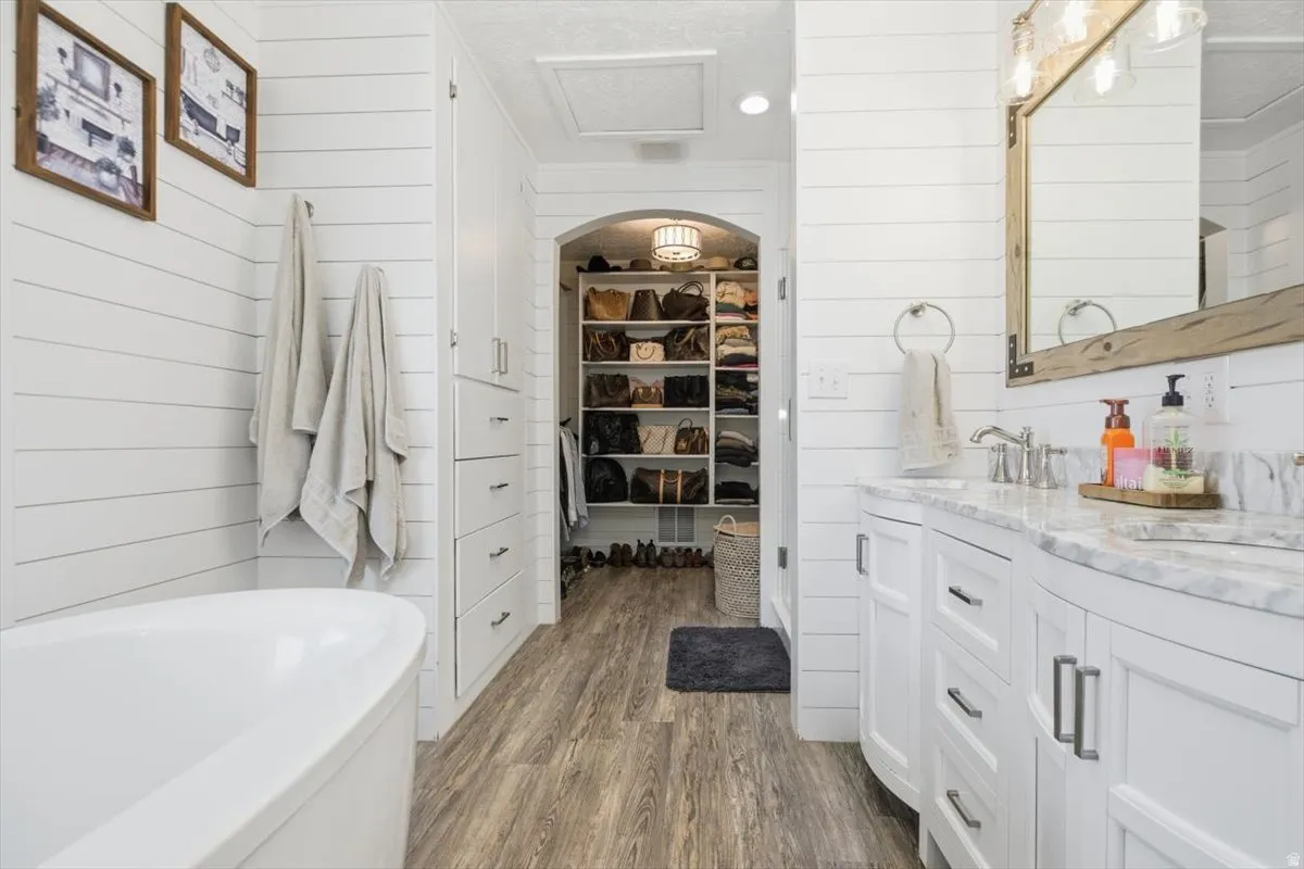 Bathroom featuring shiplap walls, wood-finish flooring, a freestanding soaking tub, and a dual vanity with a light-toned countertop