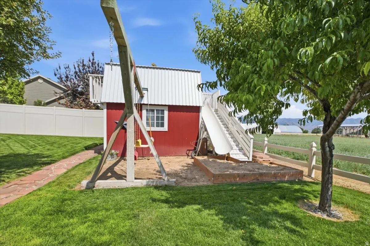 Backyard featuring a red playhouse with a white metal roof and balcony, a swing set, and an attached slide