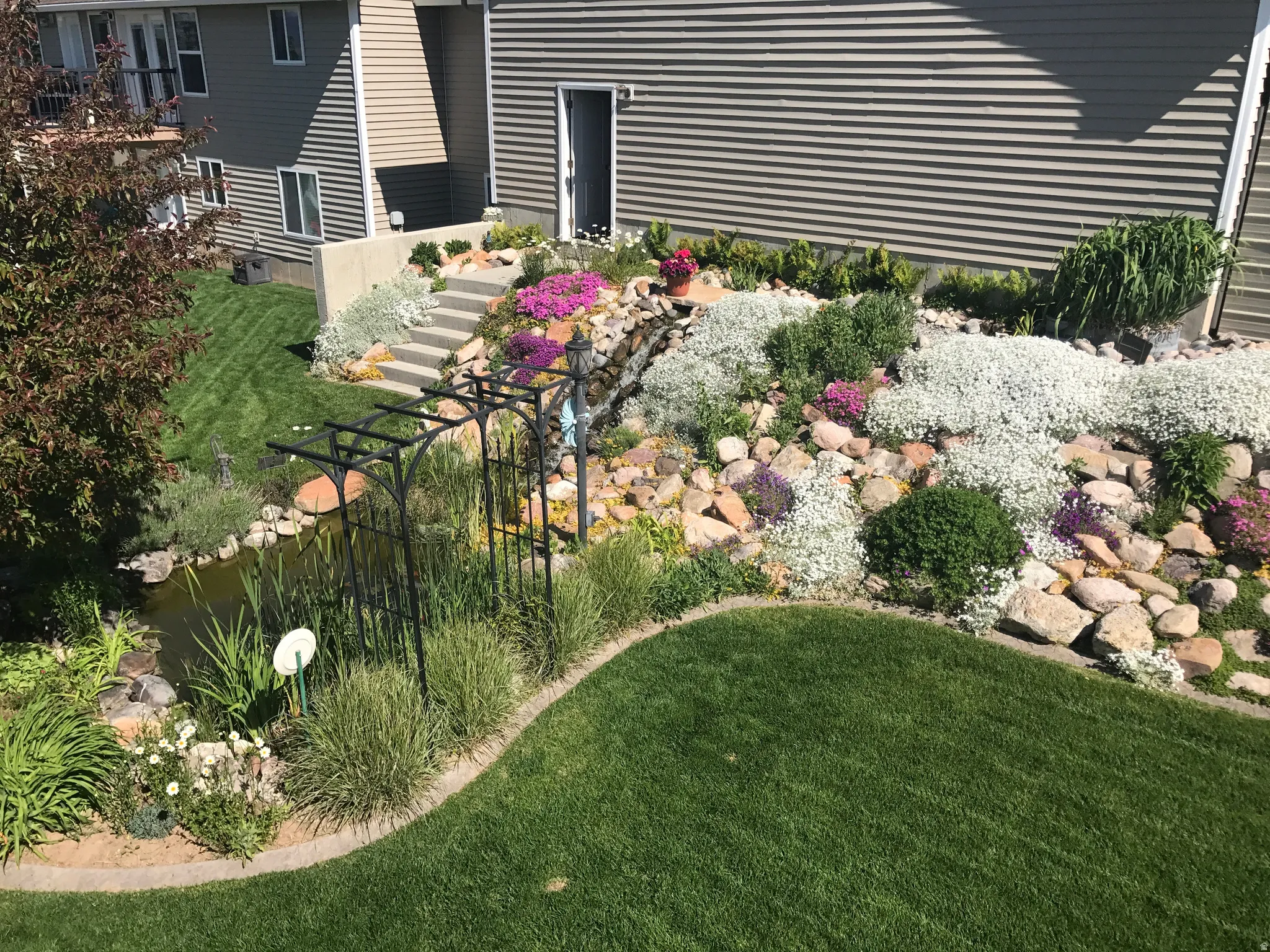 Multi-level landscaping featuring a rock garden, diverse plantings, and a water feature with an arbor