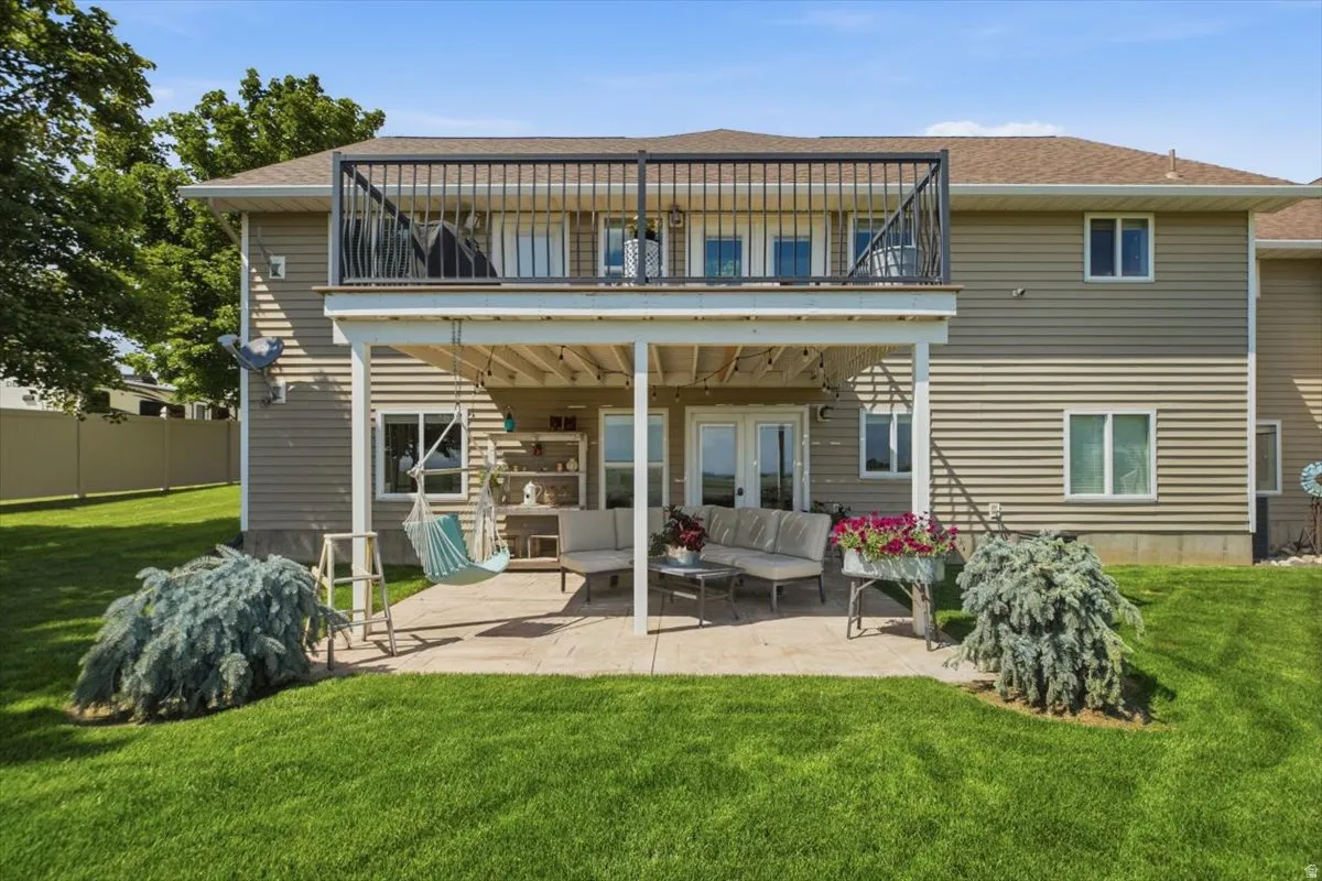 Expansive rear exterior featuring a concrete patio, covered deck, and an upper-level balcony with black metal railing