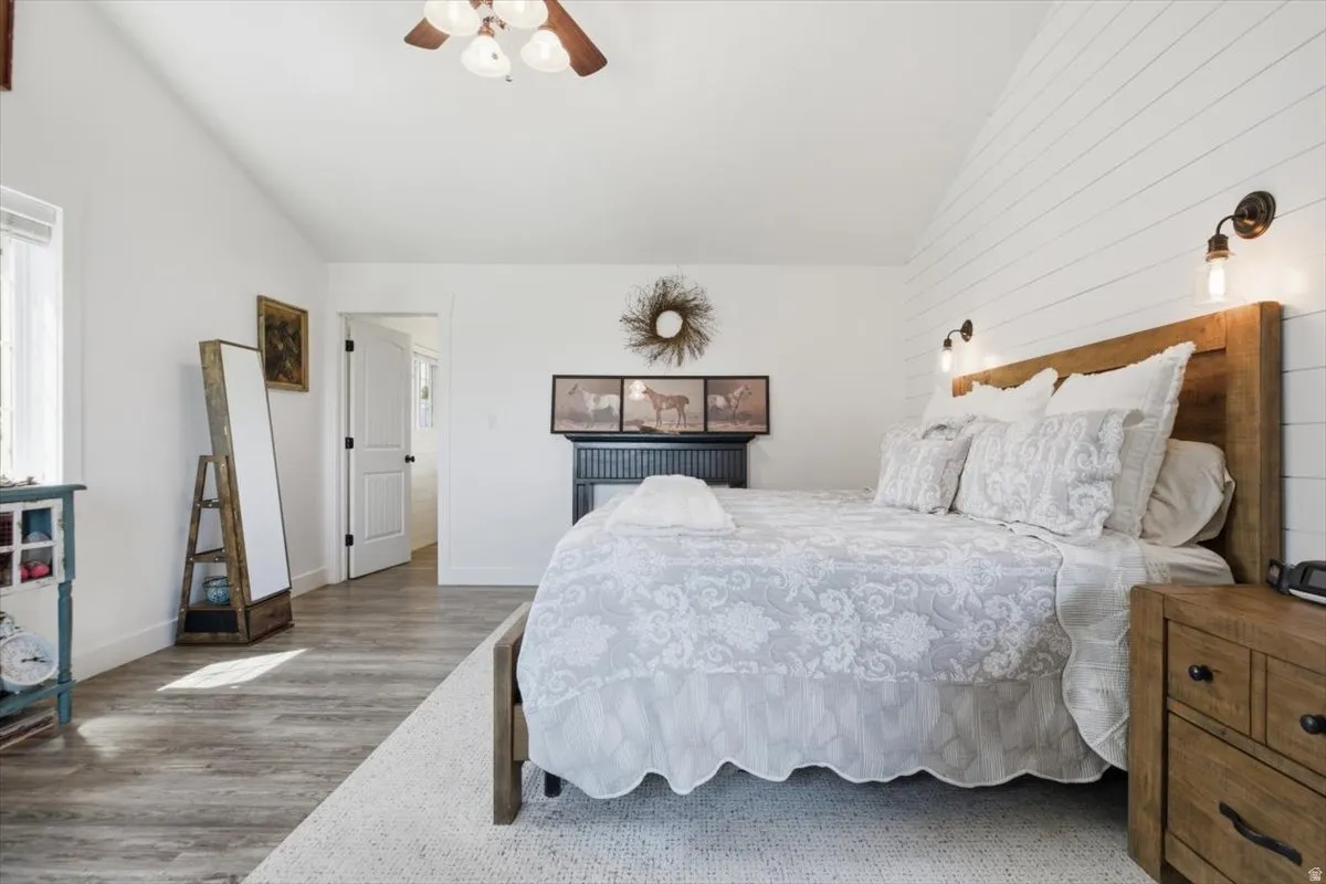 Vaulted ceiling room featuring a wood-finish flooring, white shiplap accent wall, built-in wall sconces, and a dark wood ceiling fan