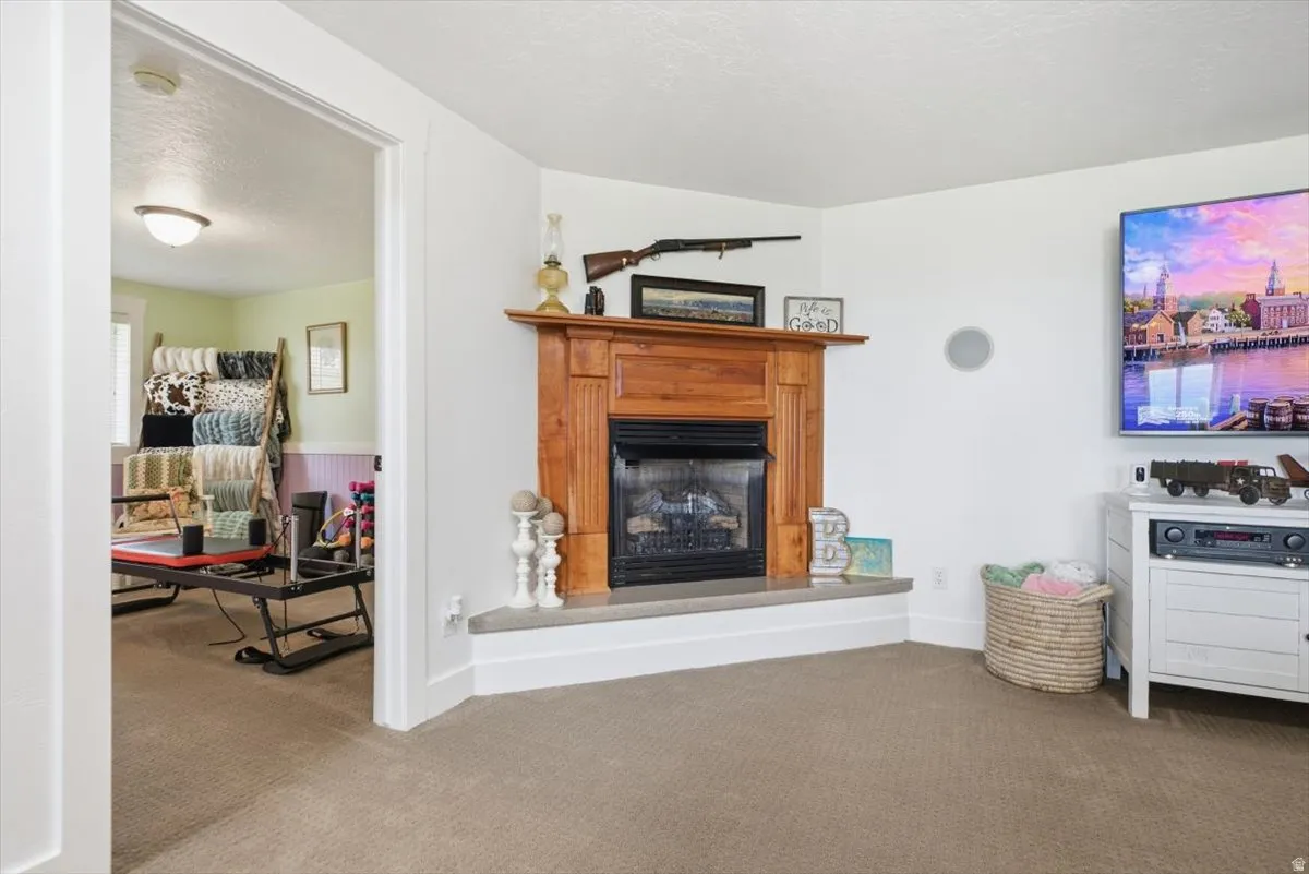 Carpeted room featuring a corner fireplace with a wood mantel and stone hearth