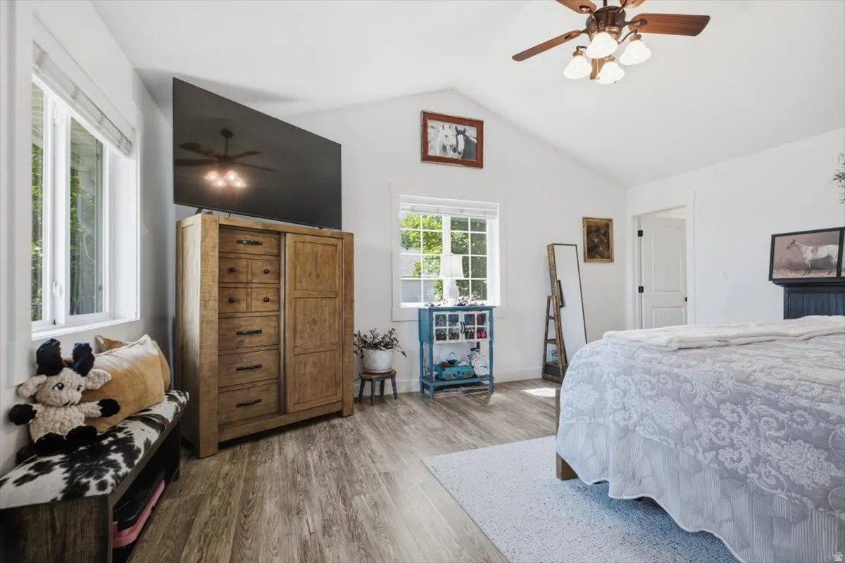 Spacious room featuring vaulted ceilings, wood-finish flooring, white walls, and a ceiling fan with integrated lighting
