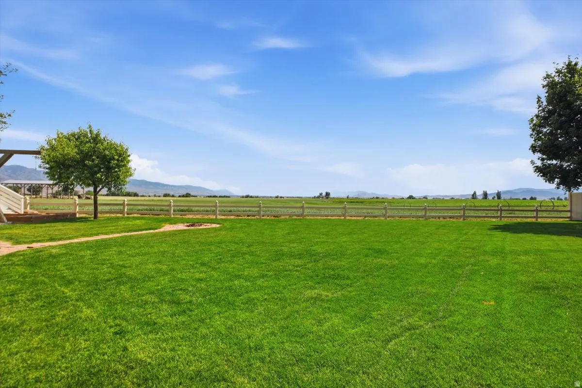 Expansive green lawn with mature trees and a wood-post fence bordering agricultural fields
