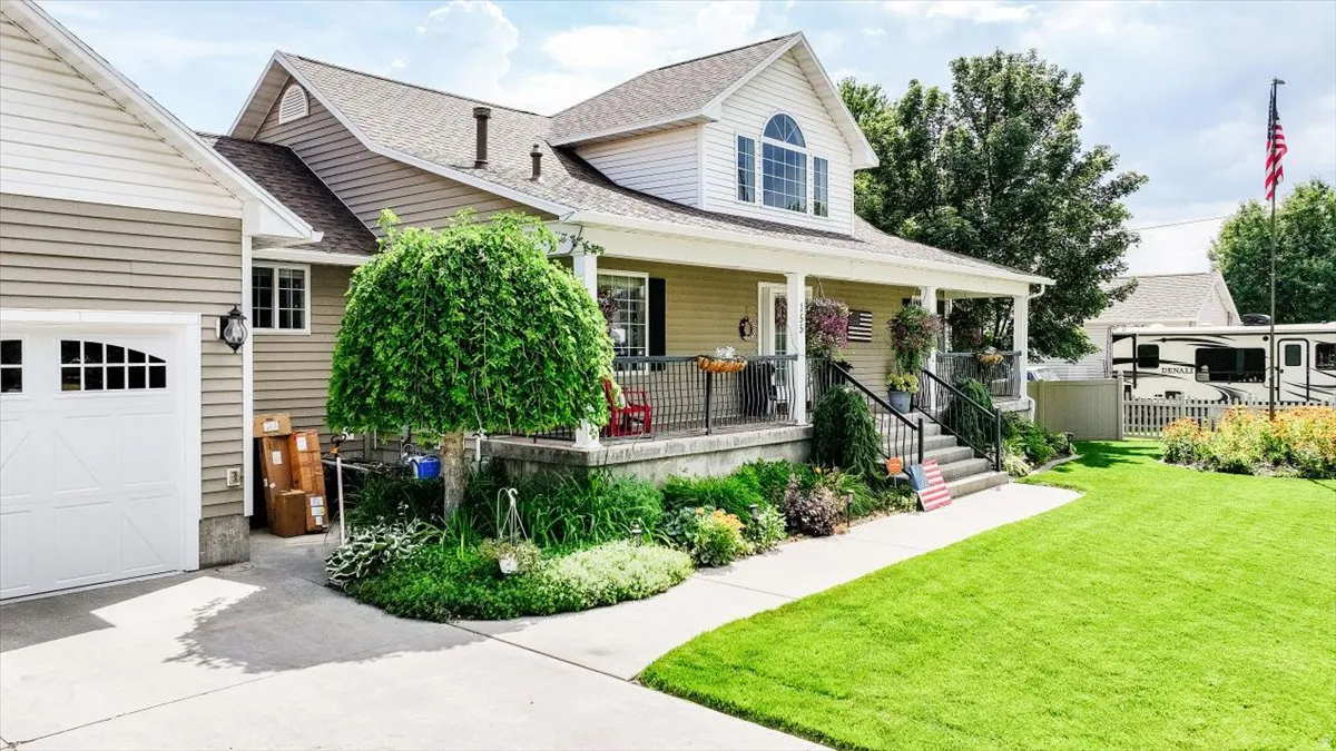 Two-story residence featuring a covered front porch, white garage door, concrete driveway, and established landscaping
