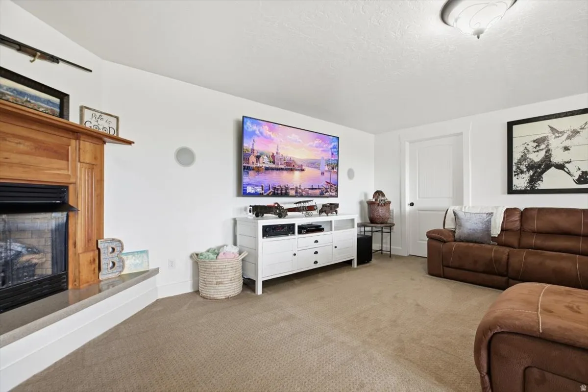 Carpeted living space featuring a wood-mantle fireplace with a hearth, white walls, and a built-in entertainment console