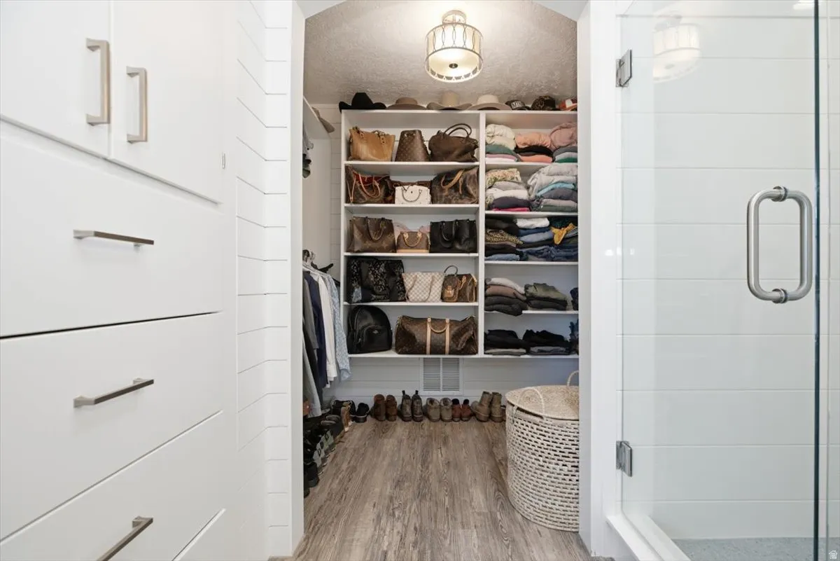 Walk-in closet with extensive built-in shelving, white cabinetry featuring modern hardware, and wood-finish flooring