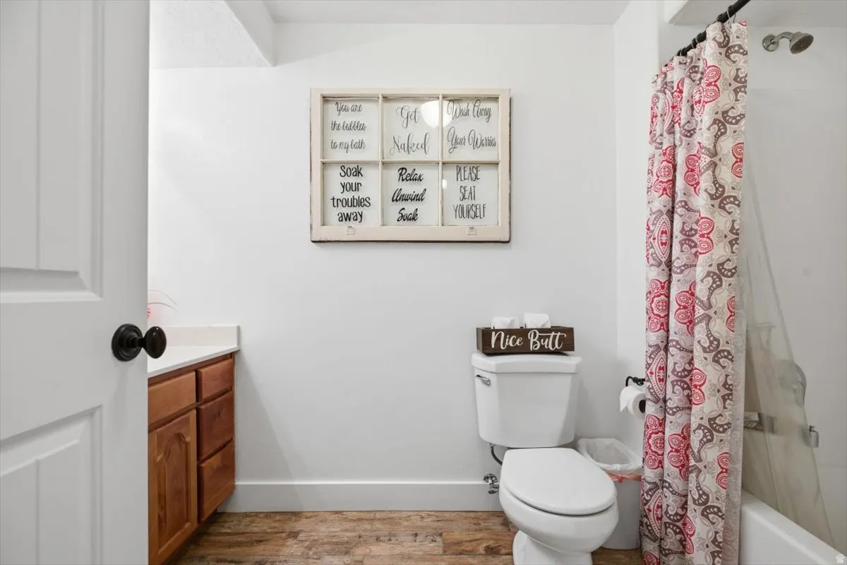 Bathroom featuring wood-finish flooring, a white vanity with wood cabinetry and a light-colored countertop, and a white toilet