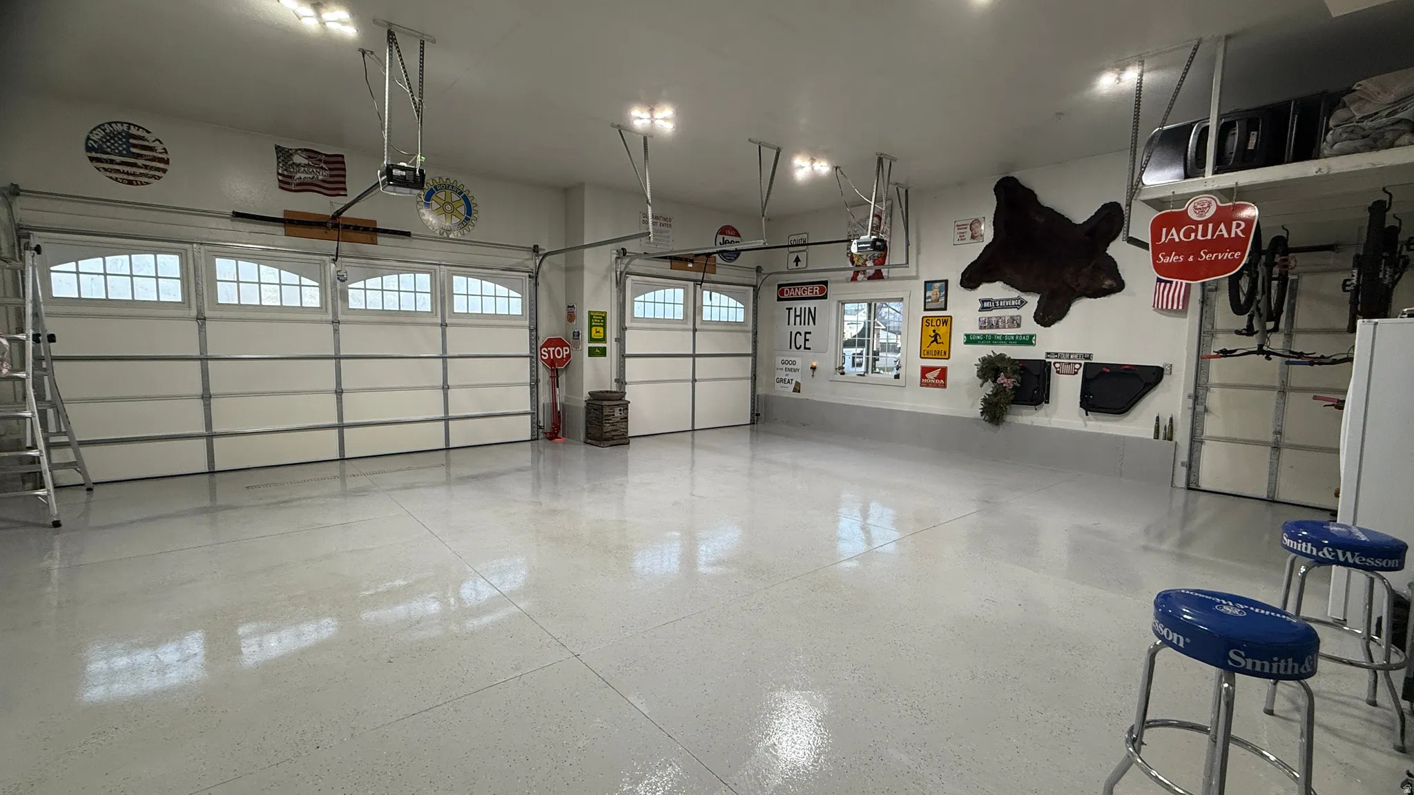 Spacious garage featuring a light-toned epoxy floor, multiple garage doors with arched window inserts, and overhead lighting
