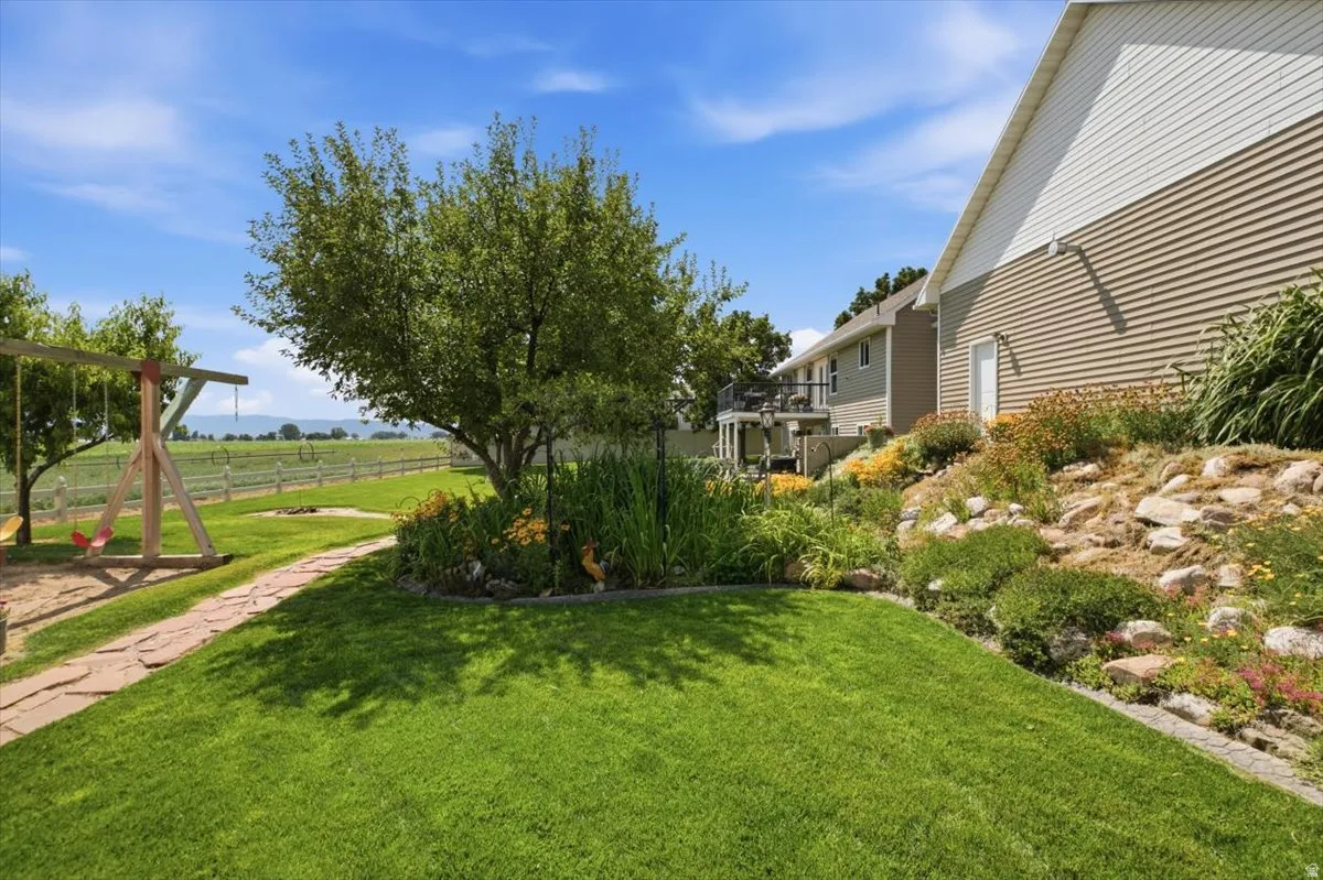 Expansive grassy yard with a flagstone pathway, mature trees, and tiered landscaping featuring decorative rocks and diverse plantings