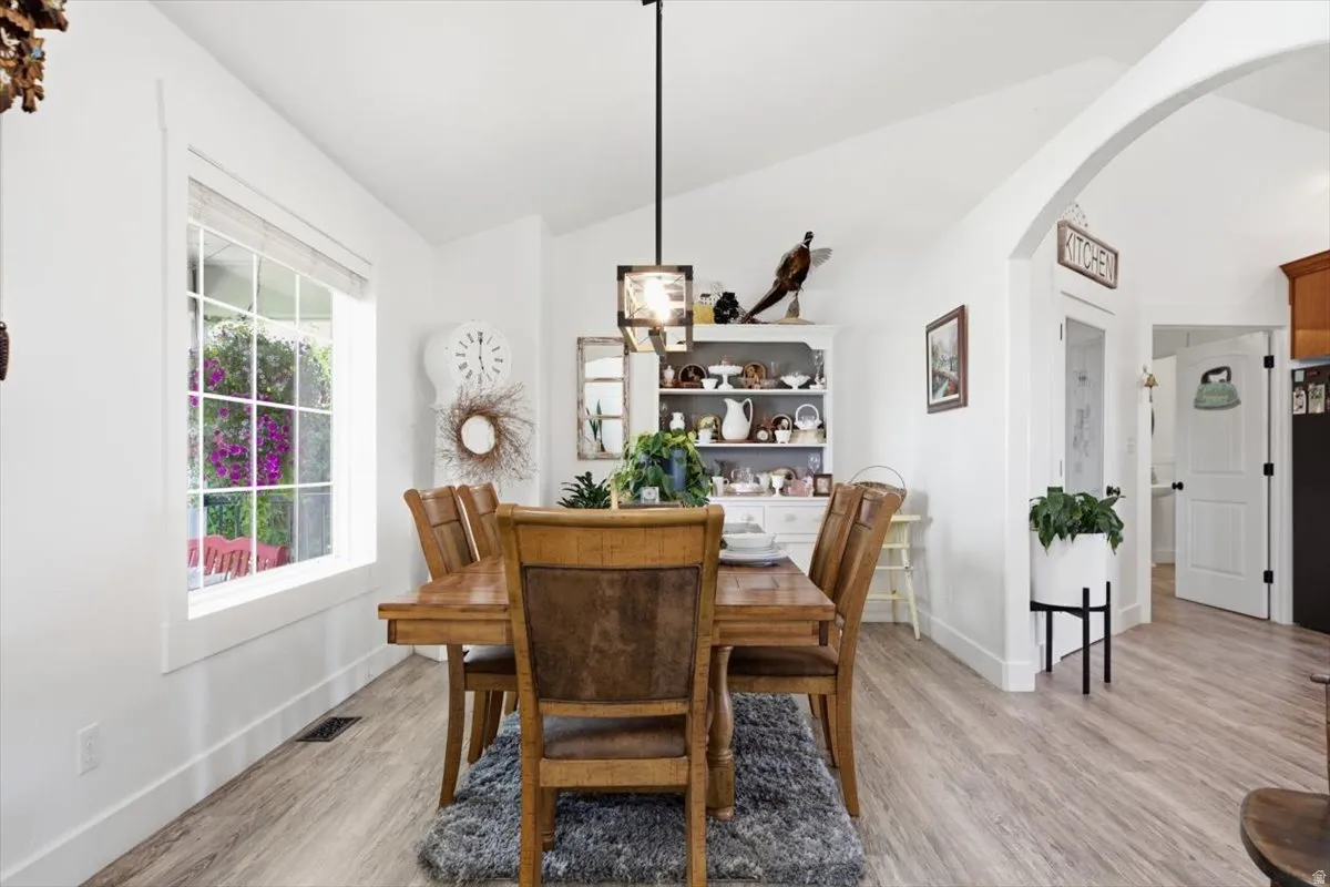 Bright dining area featuring vaulted ceilings, a large grid-pattern window, wood-finish flooring, and an arched entryway