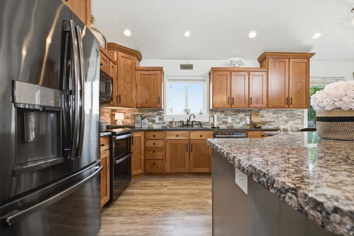 Kitchen featuring wood-finish flooring, stainless steel refrigerator, black range with double ovens, recessed lighting, and a granite-topped island