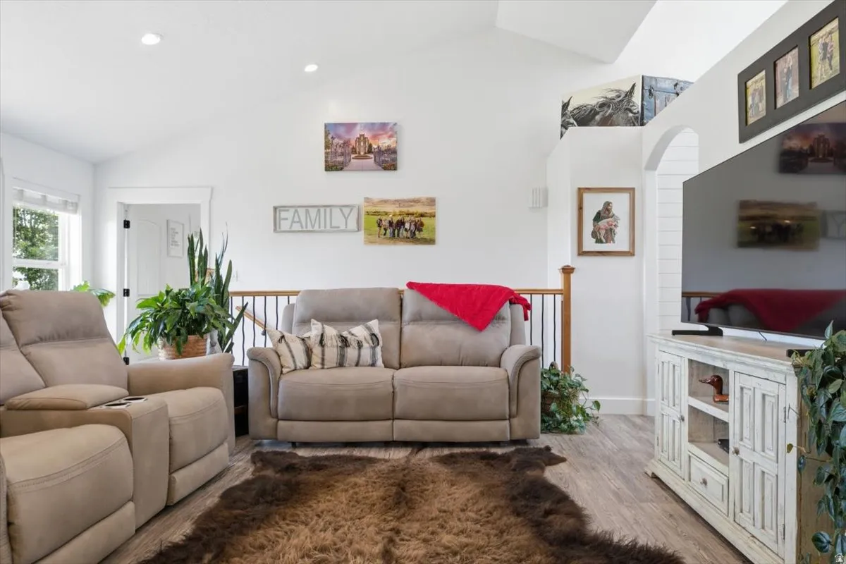 Spacious living area featuring high vaulted ceilings, recessed lighting, wood-finish flooring, a white media console with closed storage, and an open archway