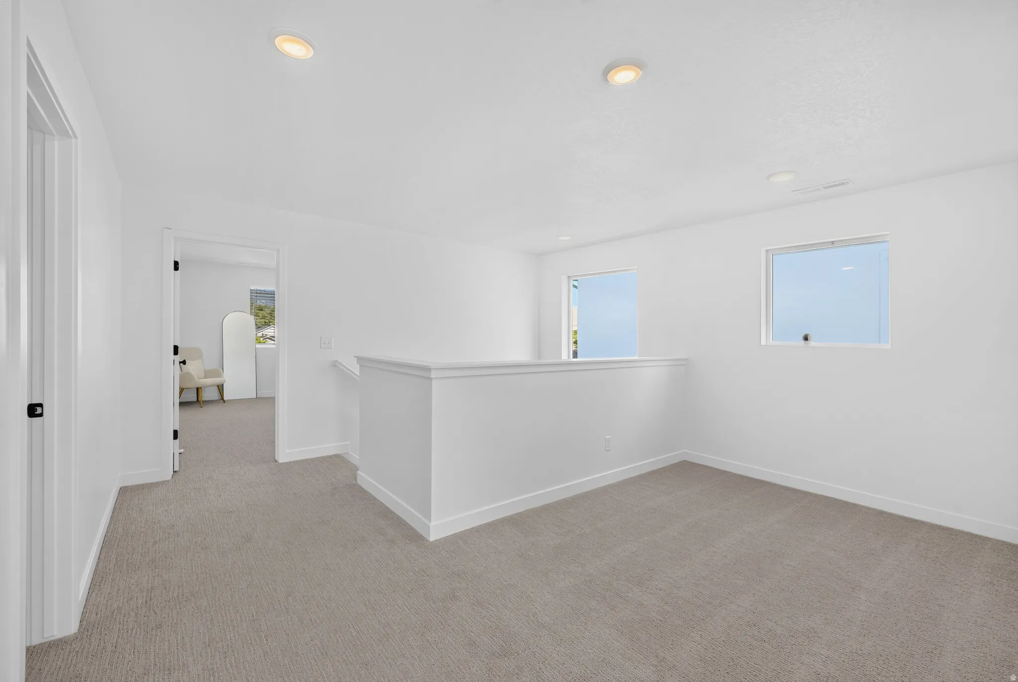 Spacious carpeted landing featuring two windows, recessed lighting, a half-wall railing, and a doorway leading to an additional interior space