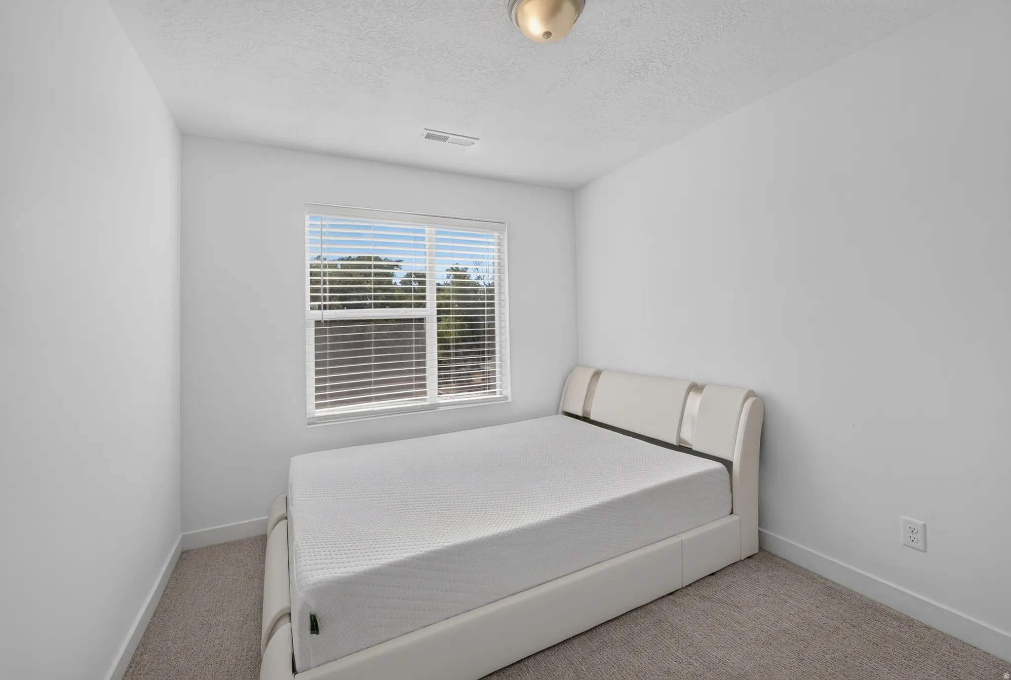 Bright room featuring a single window with horizontal blinds, neutral carpeting, and white walls