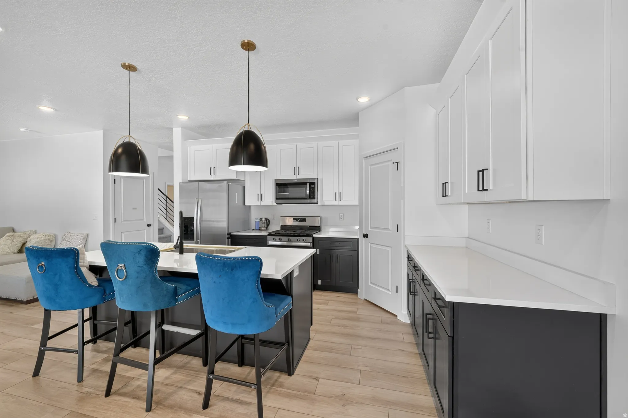 Modern kitchen featuring a large island with seating, pendant lighting, stainless steel appliances, white upper cabinetry, and dark lower cabinetry