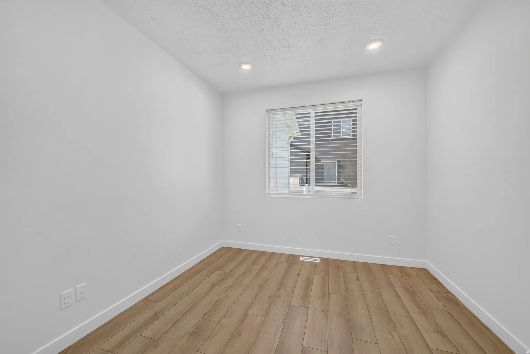 Room with light wood-finish flooring, white walls, and a window with blinds