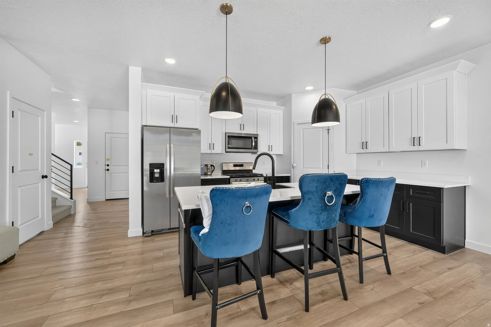 Modern kitchen featuring an island with counter seating, stainless steel appliances, white upper cabinetry, and dark lower cabinetry